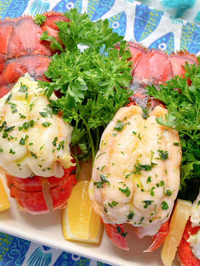 butterflied air fryer lobster tails on a platter with fresh parsley and lemon wedges