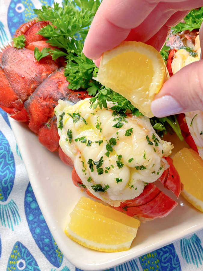 squeezing a lemon wedge over an air fryer lobster tail