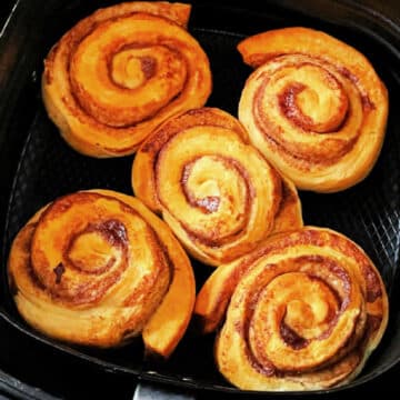 five freshly baked cinnamon rolls in the air fryer basket