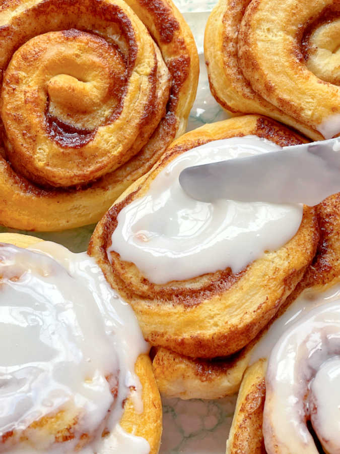 topping the air fryer cinnamon rolls with cream cheese frosting