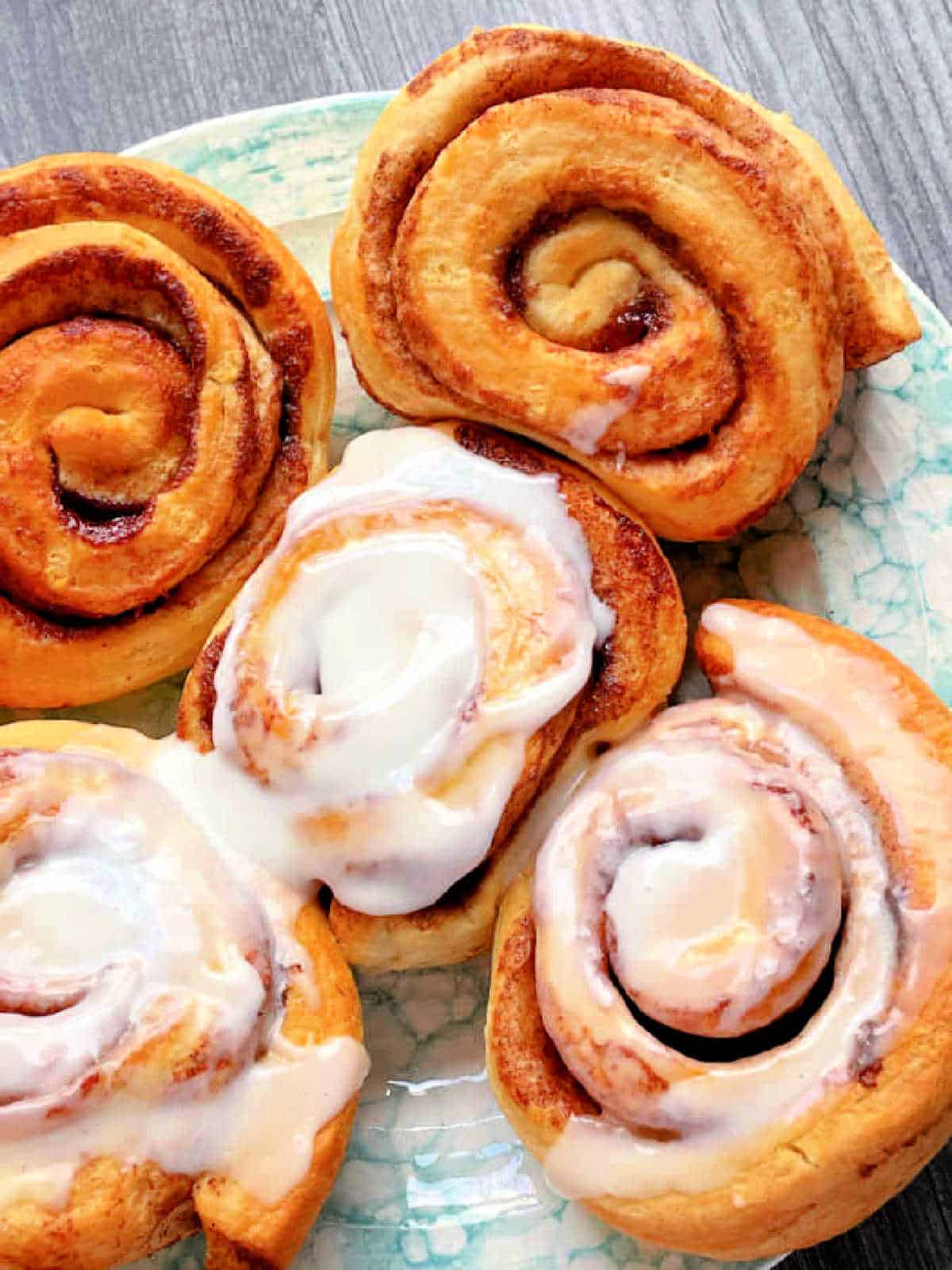 five air fried cinnamon rolls on a plate with three frosted and two unfrosted
