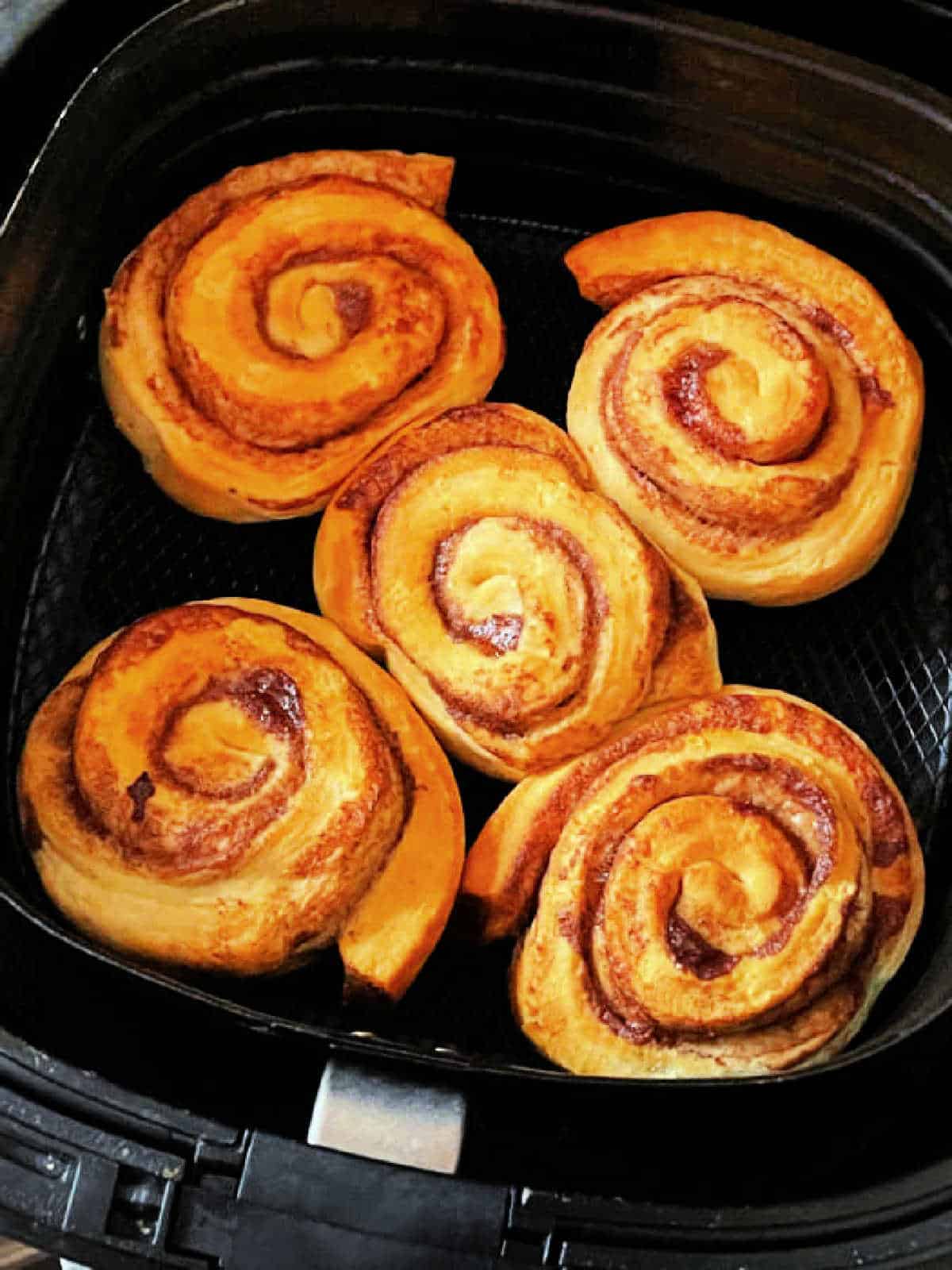 five fully baked cinnamon rolls in the air fryer basket