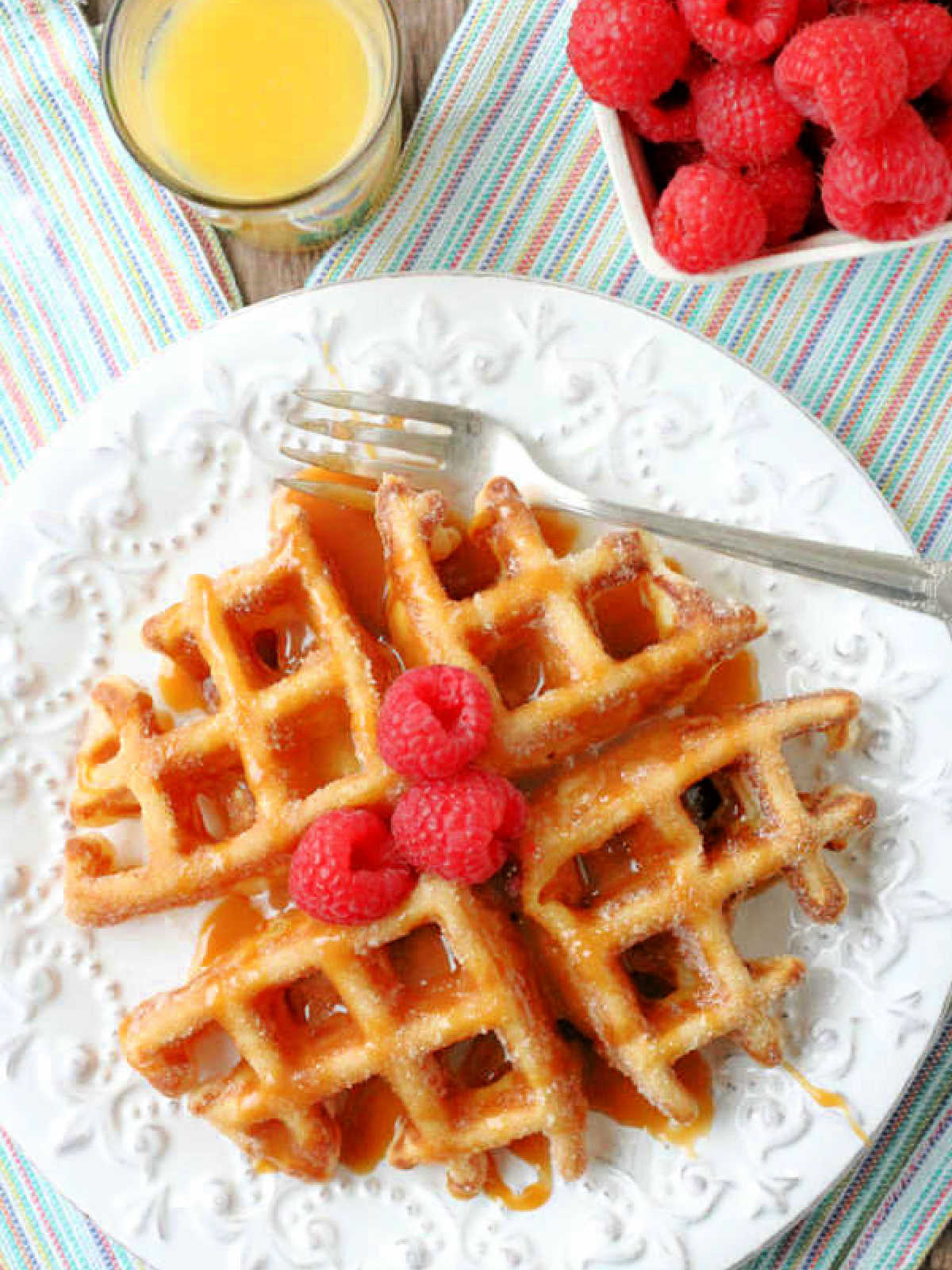 plated churro waffles with a glass of orange juice and a pint of fresh raspberries on the side