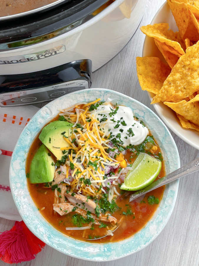 taco soup with chicken topped with avocado, lime, cheese and sour cream