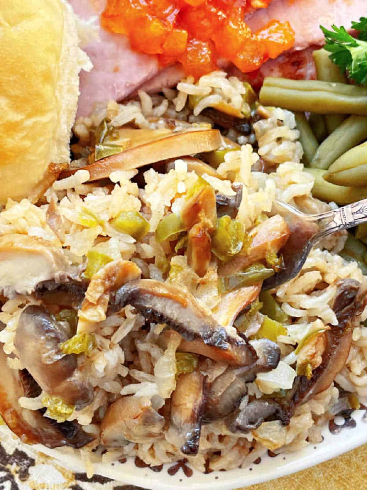 showing the mushroom rice pilaf plated with ham, green beans and a dinner roll
