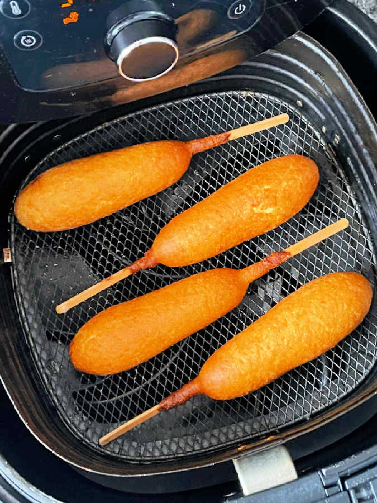 four freshly fried corn dogs in the air fryer basket