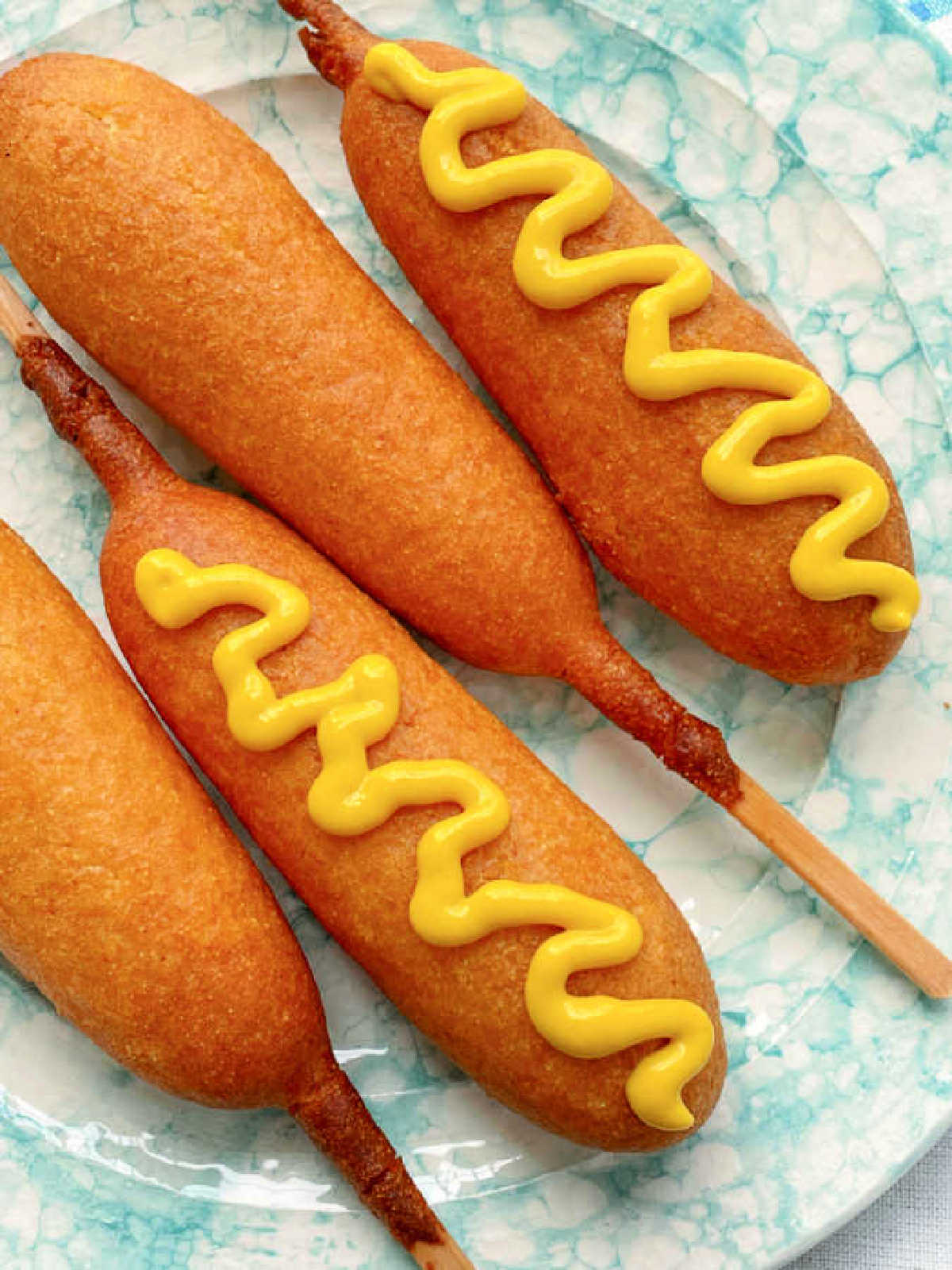 four plated corn dogs and two of them topped with yellow mustard