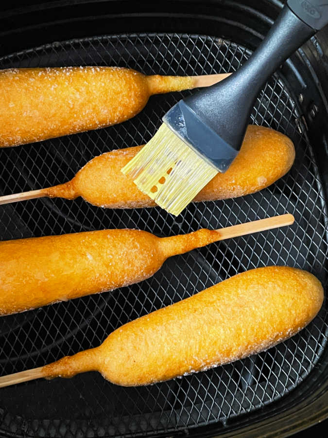 corn dogs in basket of air fryer being coated with oil