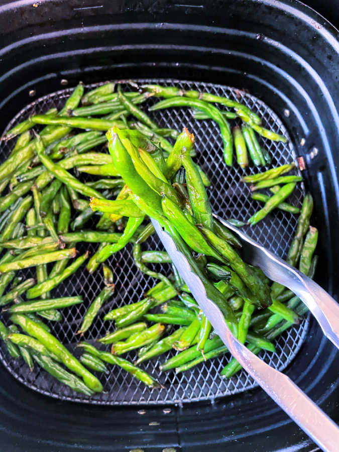 picking up green beans from air fryer basket with tongs