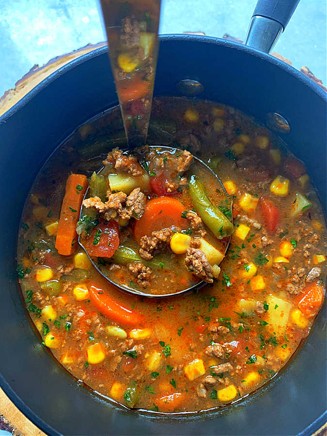 a ladle full of campfire stew in the pot that it was cooked in