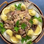 slow cooker lamb shoulder garnished with artichoke hearts and lemon slices on a serving platter