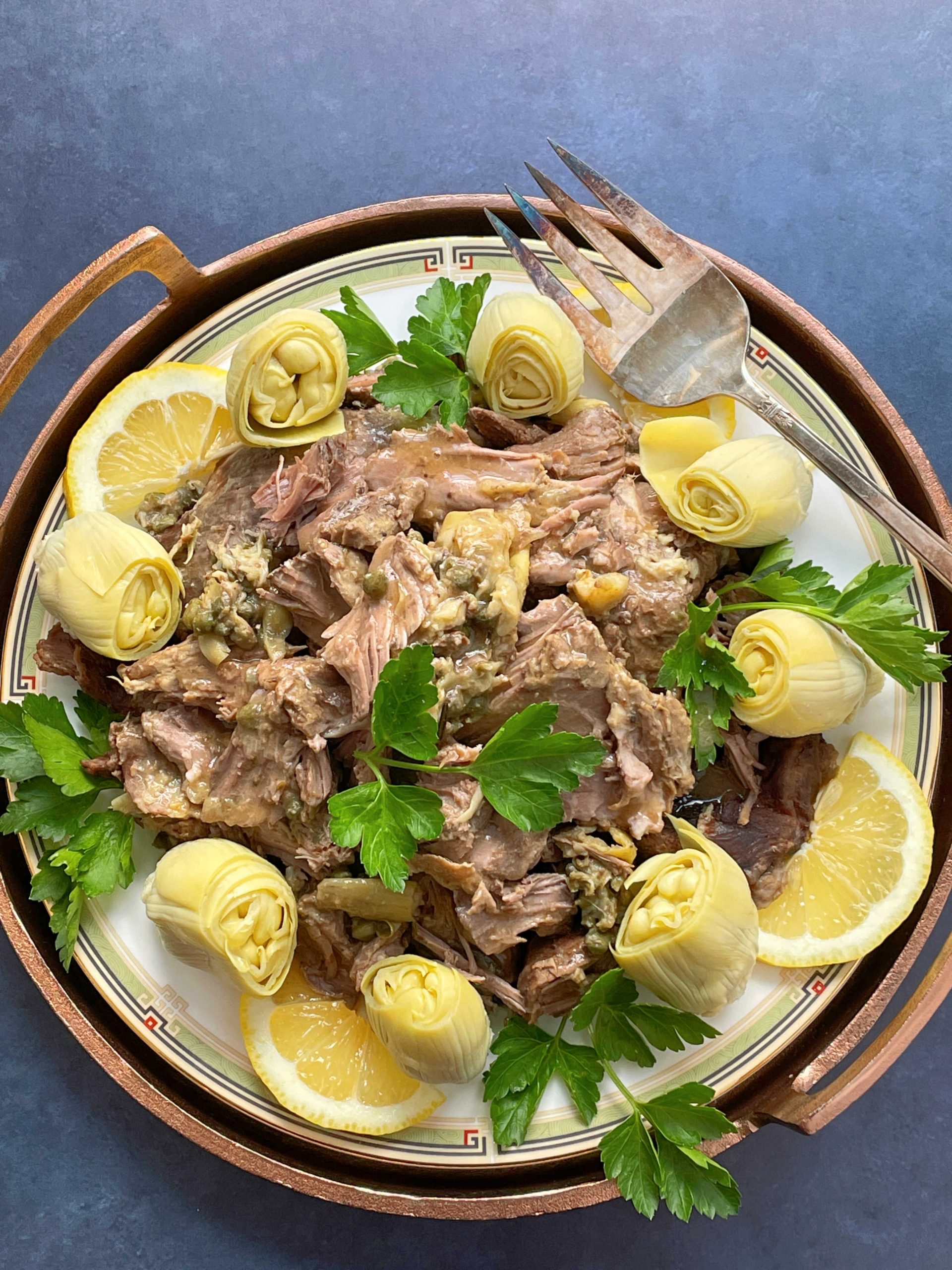 slow cooker lamb shoulder on platter garnish of artichoke hearts and lemon slices