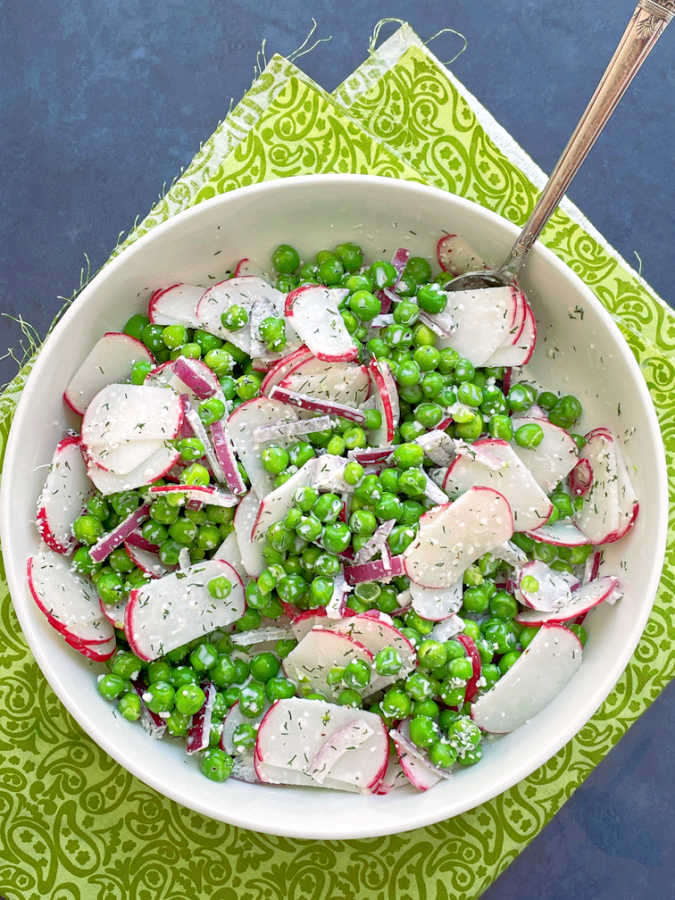 English pea salad in white serving bowl with sliced radish and chopped red onion