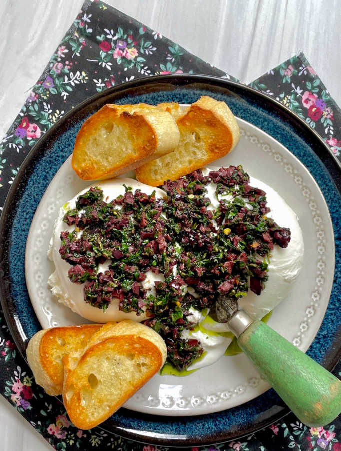 burrata bruschetta on a plate with serving knife and baguette slices