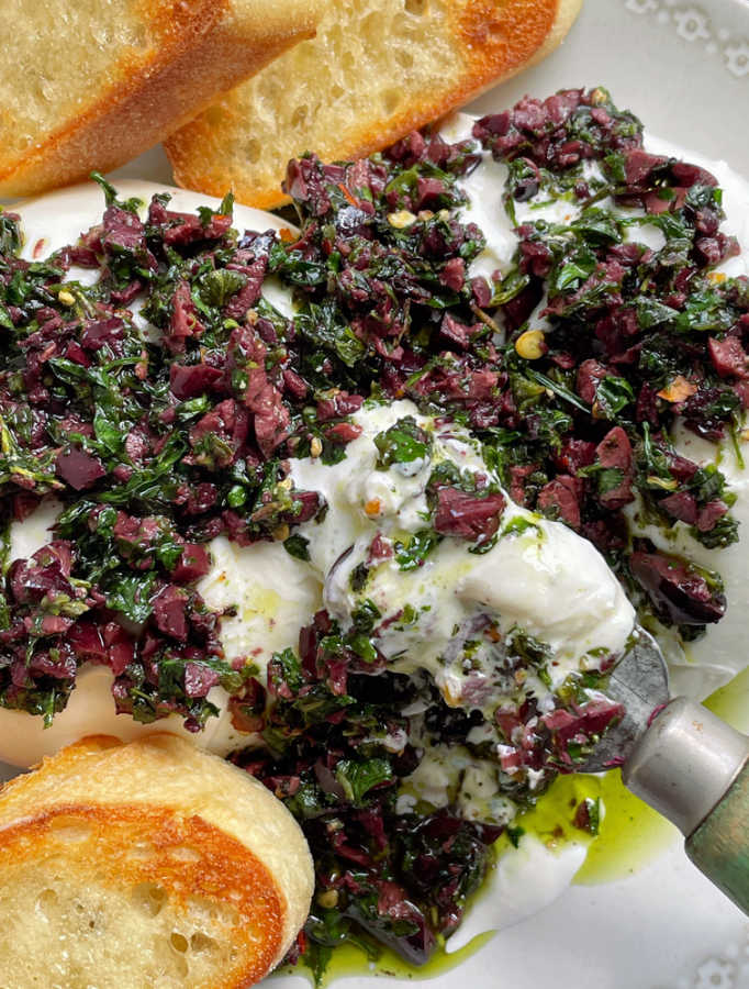 scooping up some burrata cheese and olive relish onto a bread slice