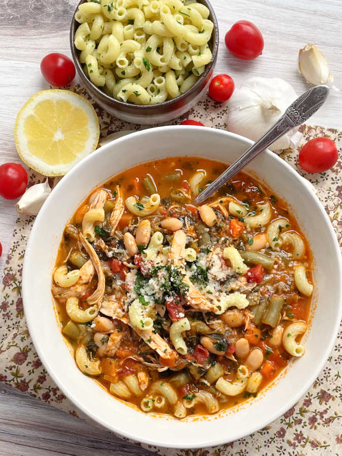 chicken minestrone soup in a bowl with a small bowl of cooked pasta on the side