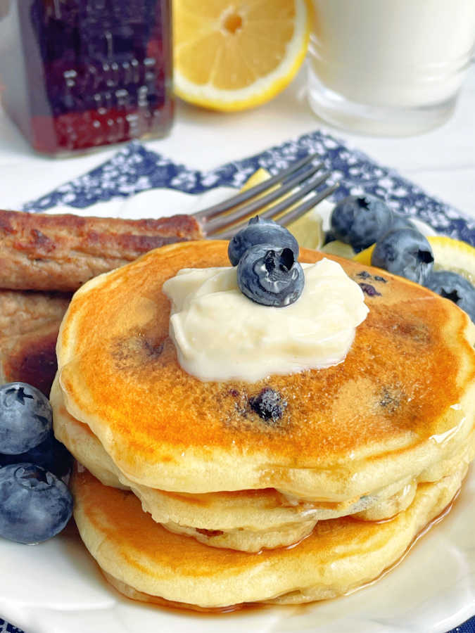 lemon blueberry pancakes plated with syrup and a glass of milk in the background