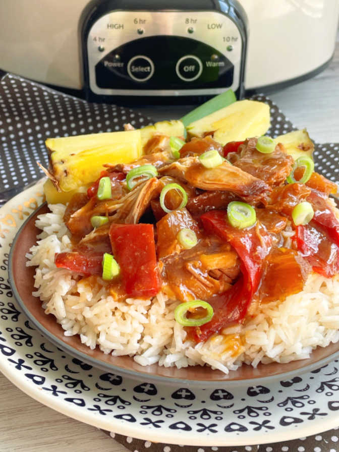 sweet Hawaiian crock pot chicken plated in front of a slow cooker and garnished with fresh pineapple