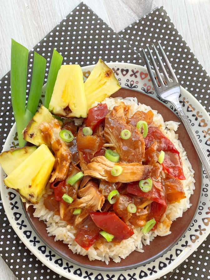 sweet Hawaiian crock pot chicken plated on top of rice and garnished with green onions and fresh pineapple