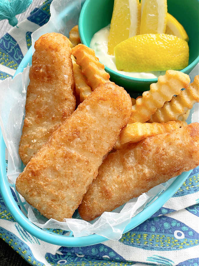 air frozen fish and french fries in a basket with lemon wedges and tartar sauce