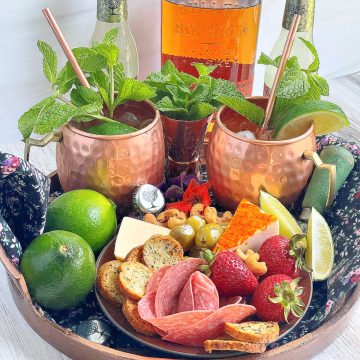 bourbon mules pictured with a plate of charcuterie and a bottle of Bulleit bourbon