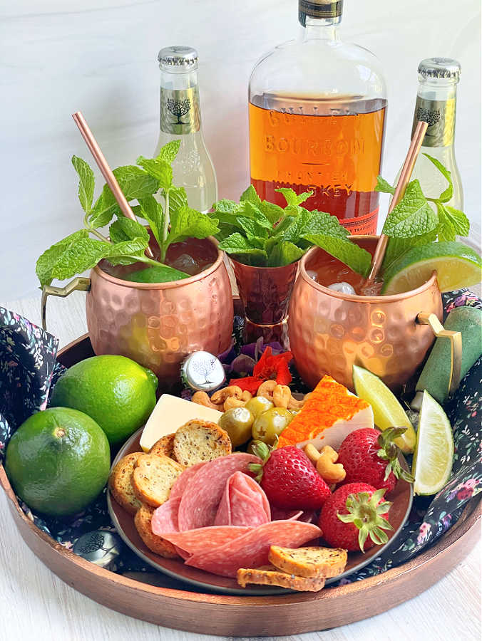 bourbon mules pictured with charcuterie and a bottle of Bulleit bourbon