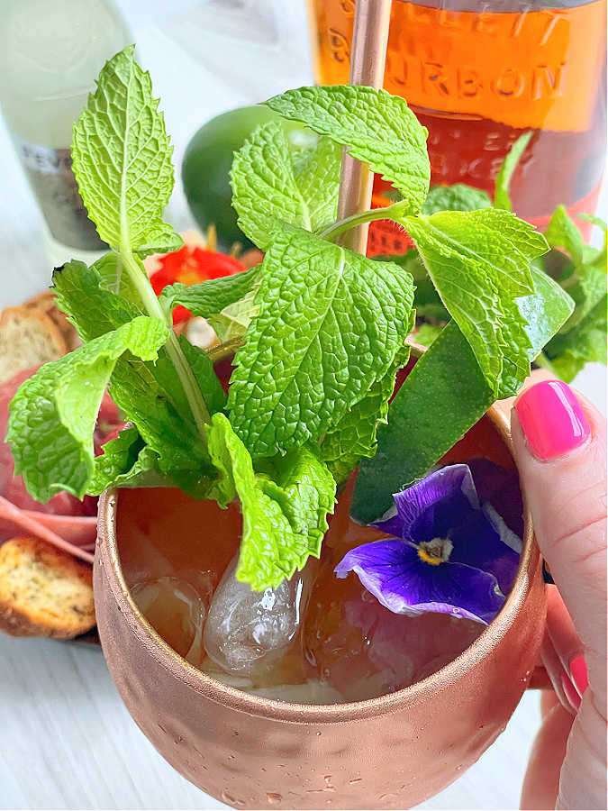 taking a drink of an ice cold bourbon mule garnished with an edible purple flower