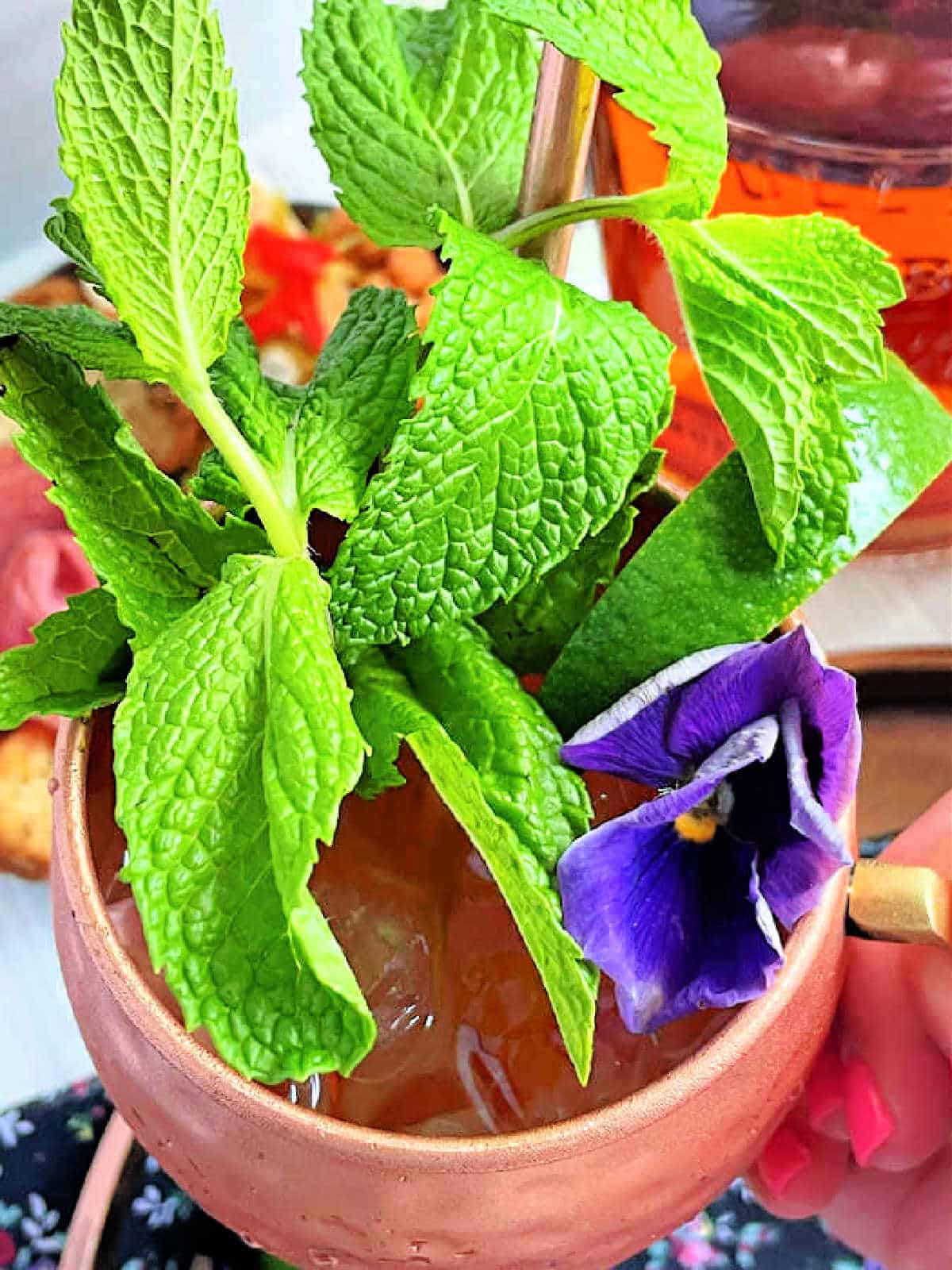 bourbon mule garnished with mint and an edible purple flower