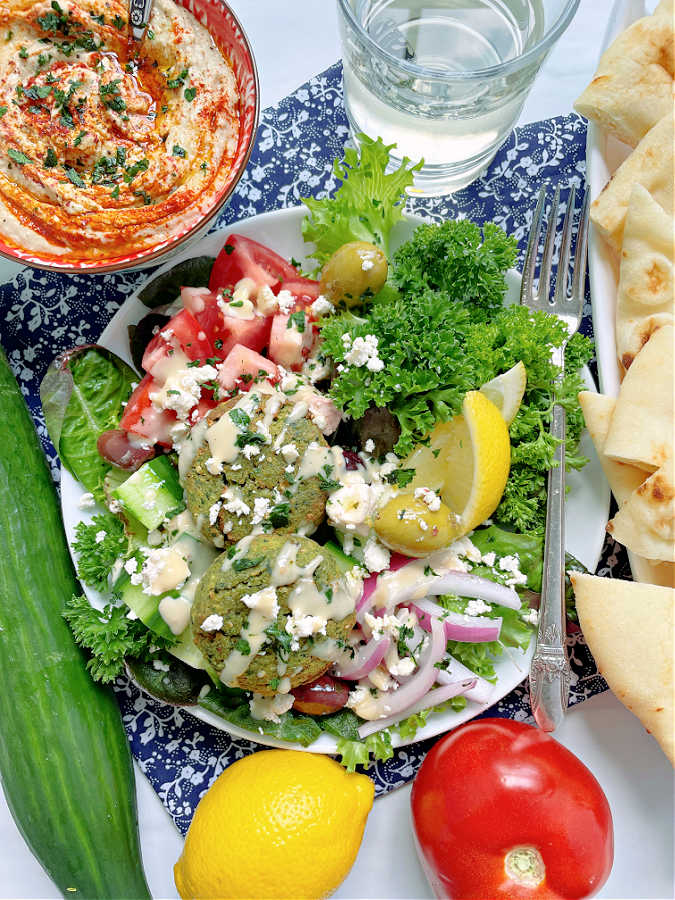 air fryer falafel plated with a chopped salad with a glass of white wine on the side, plus pita bread triangles and a bowl of hummus