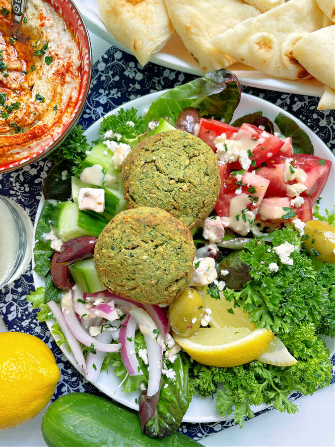 air fryer falafel plated with a Greek inspired chopped salad (cucumbers, tomatoes, onion, feta and olives, parsley, plus some naan bread and hummus for dipping