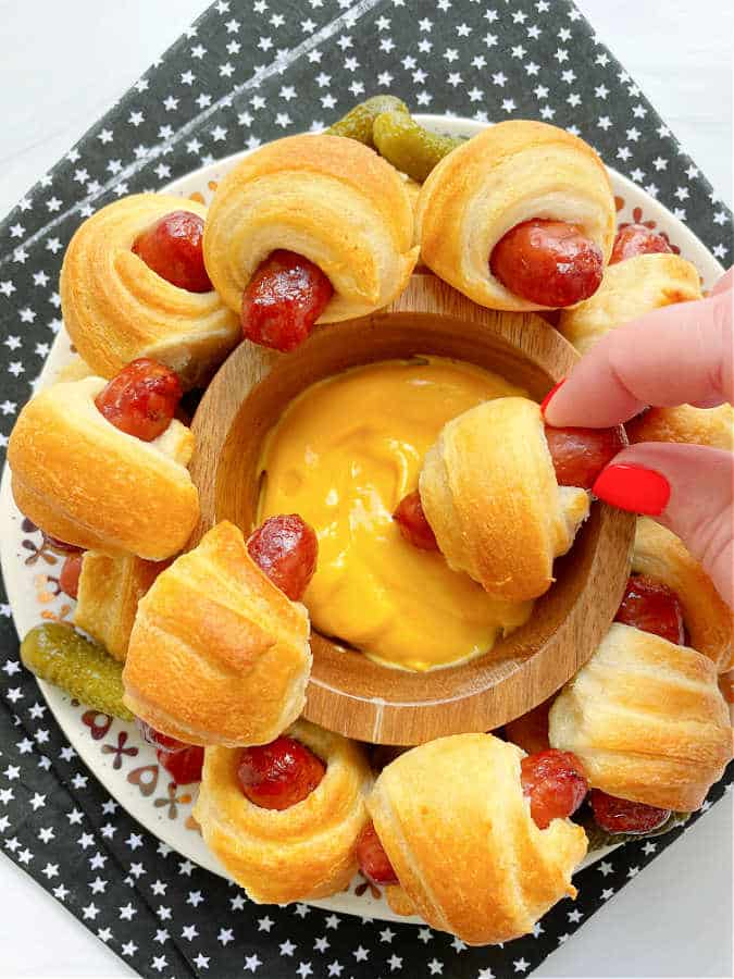 dipping an air fryer pig in a blanket into a cheesy mustard sauce