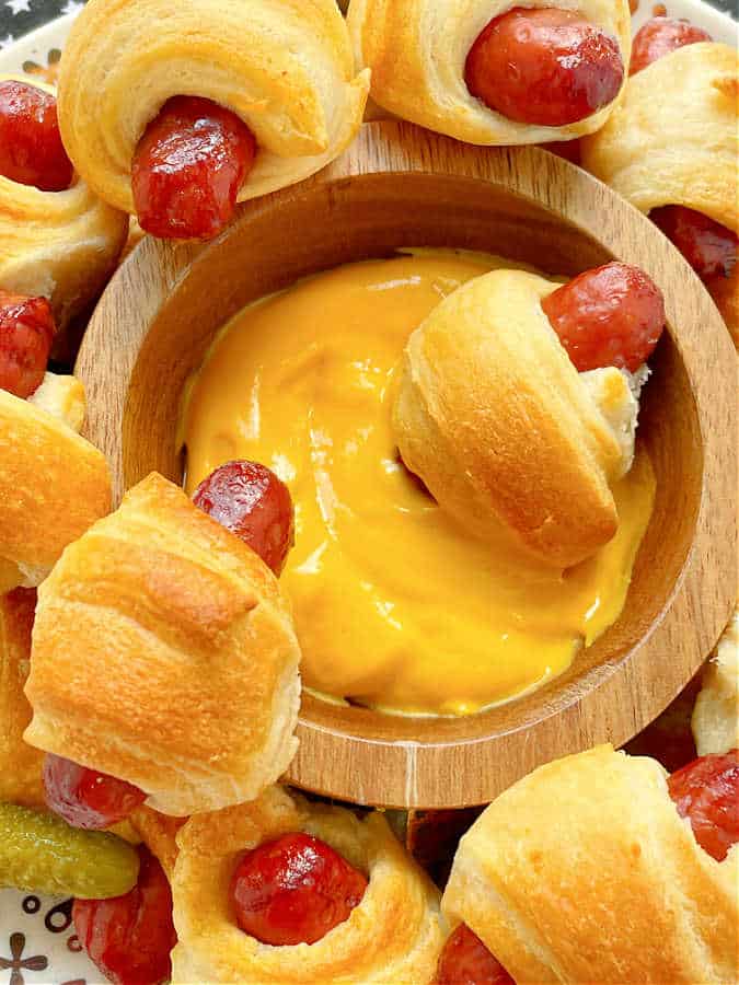 a close up of two air fryer pigs in a blanket being dipped into a bowl of cheese sauce