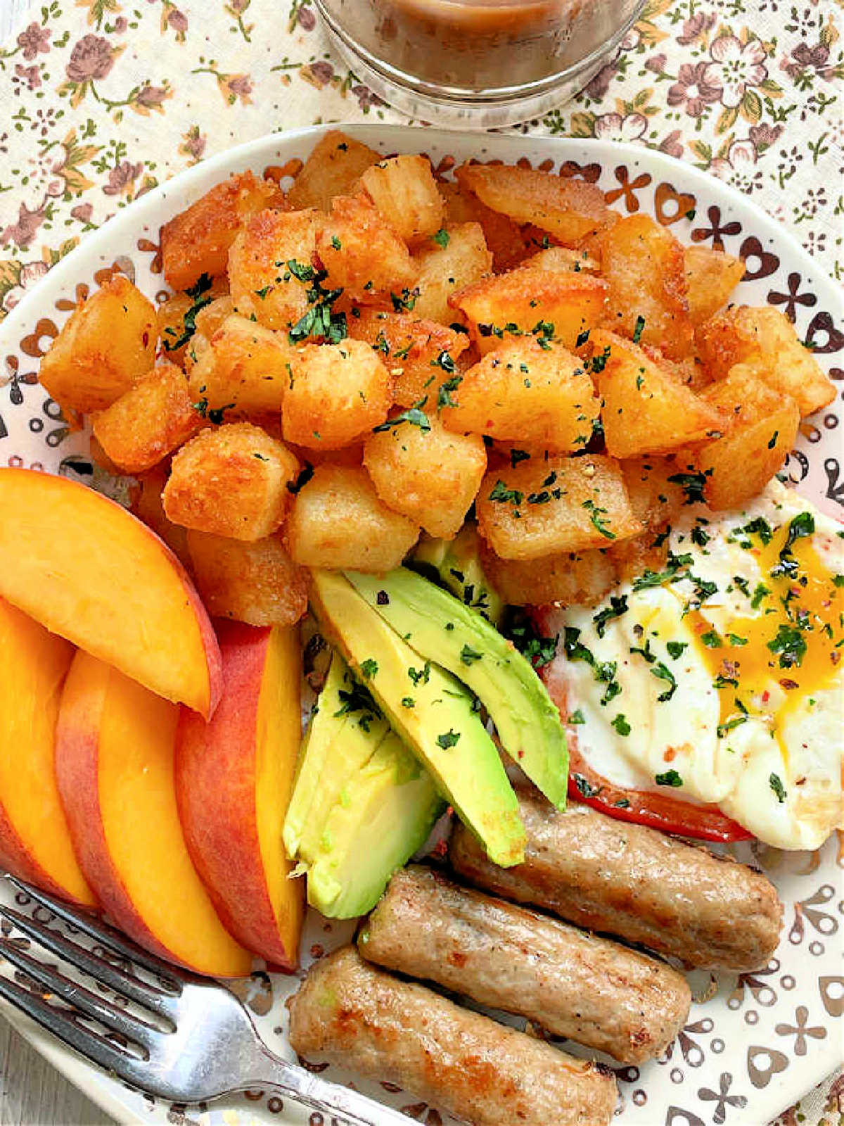 breakfast potatoes plated with a runny egg, sliced avocado, air fryer breakfast sausage and peaches