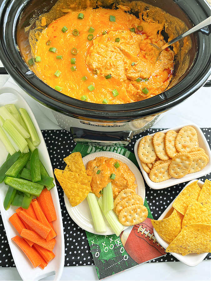 crock pot buffalo chicken dip ready to serve with a platter of vegetables plus crackers and tortilla chips