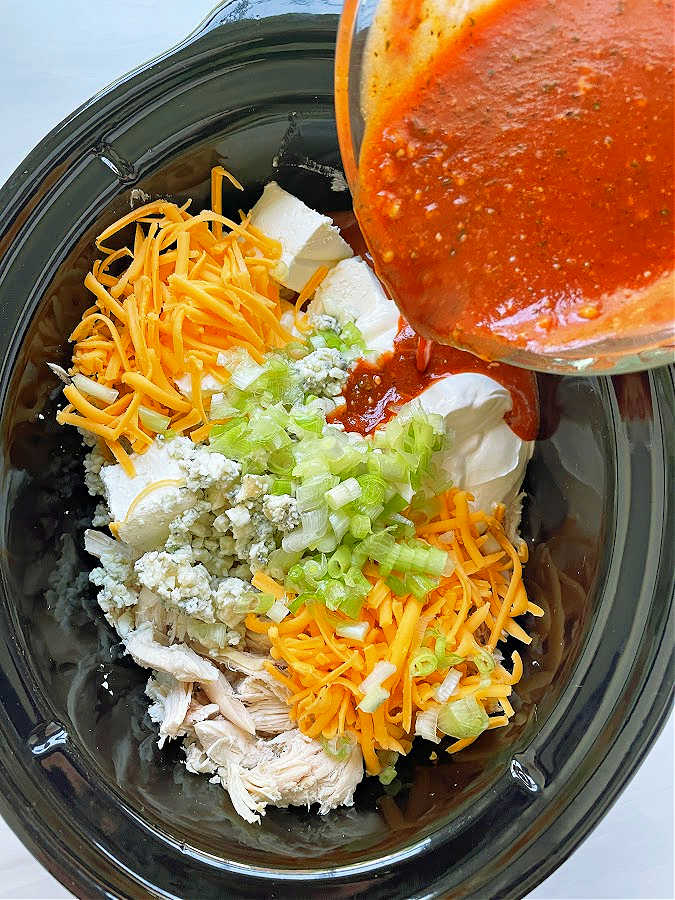 all of the ingredients for buffalo chicken dip in the crock pot insert