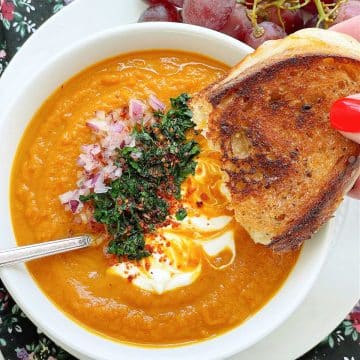 dipping a half a grilled cheese into a bowl full of slow cooker pumpkin soup