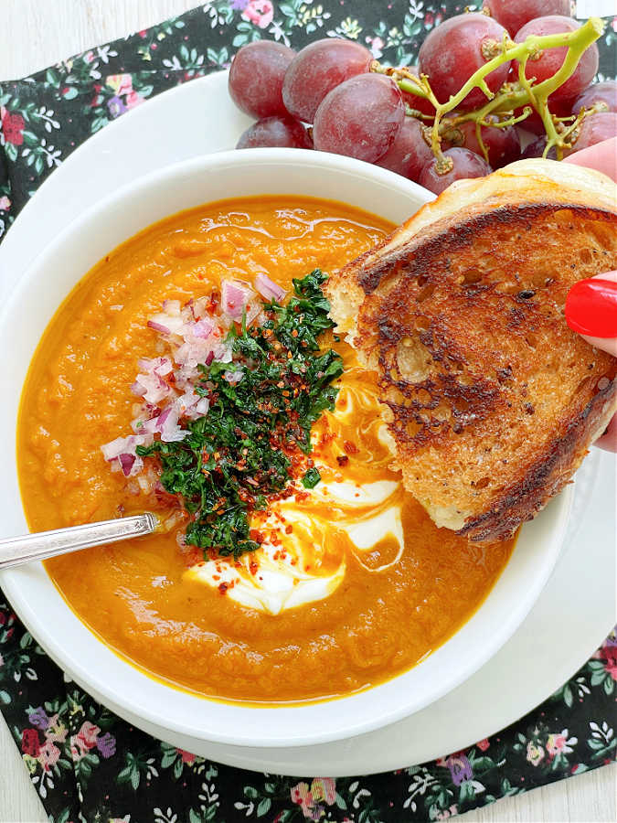 dipping a half a grilled cheese sandwich in a bowl of slow cooker pumpkin soup