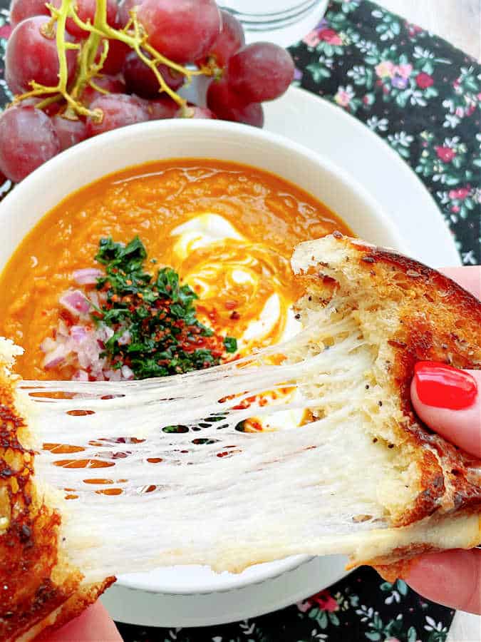 pulling apart a grilled cheese sandwich so it's ready to dip into the bowl of slow cooker pumpkin soup