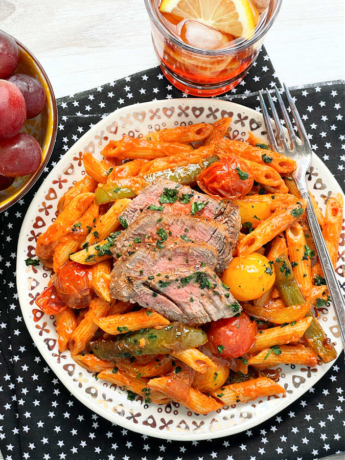 steak pasta plated with a bowl of grapes and a glass of iced tea on the side