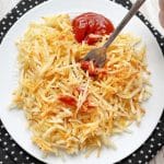 frozen shredded hash brown potatoes cooked in the air fryer and topped with ketchup on a white plate