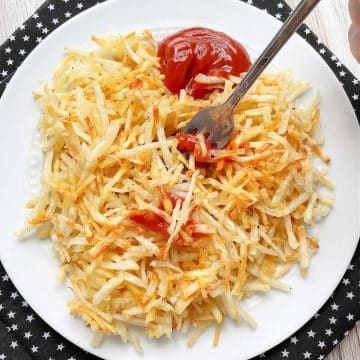 frozen shredded hash brown potatoes cooked in the air fryer and topped with ketchup on a white plate