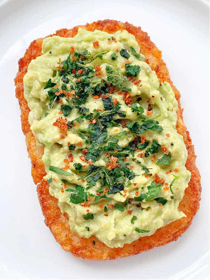 air fryer hashbrown potato pattie topped with mashed avocado and fresh herbs