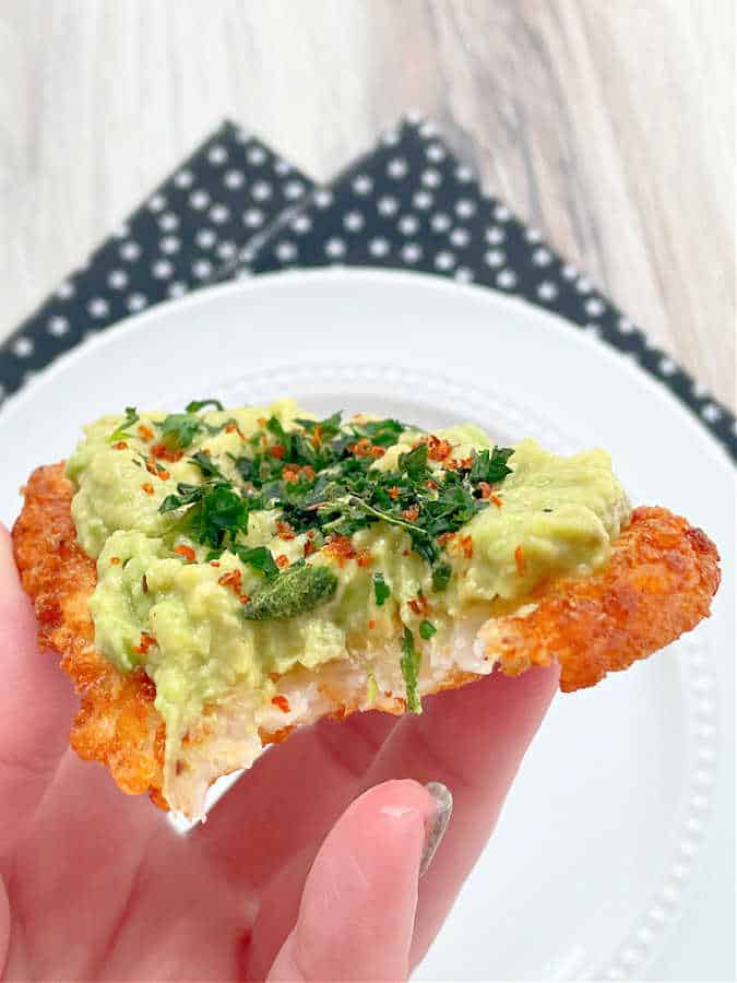 taking a bite of an air fried hashbrown pattie topped with mashed avocado