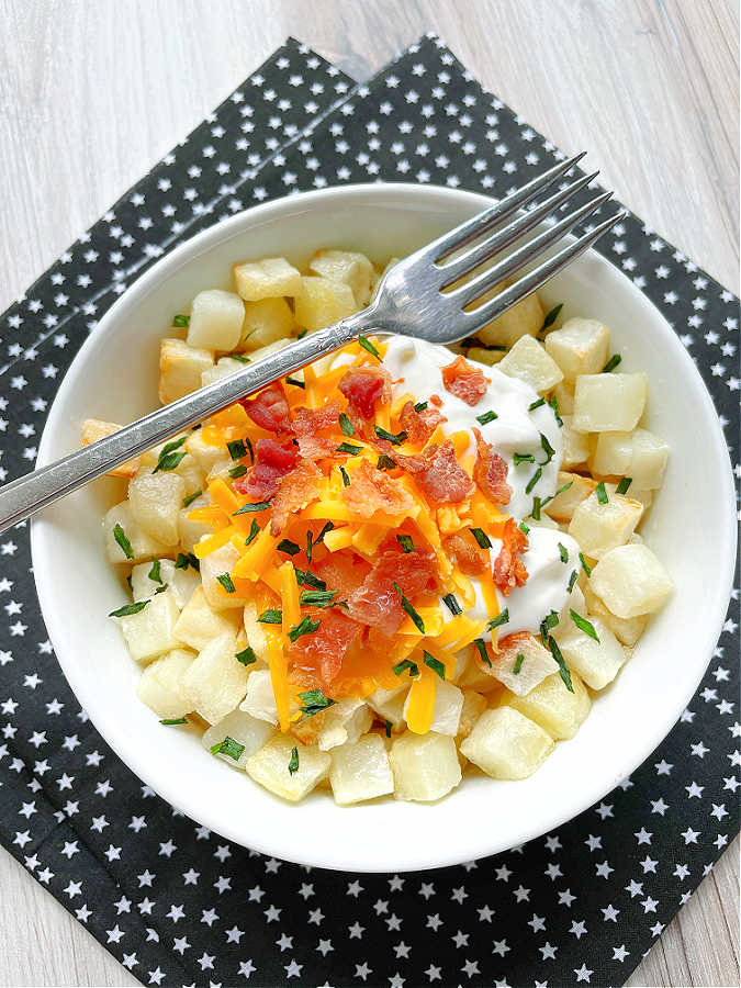 air fryer cubed hashbrowns in a bowls topped with bacon, cheese and sour cream