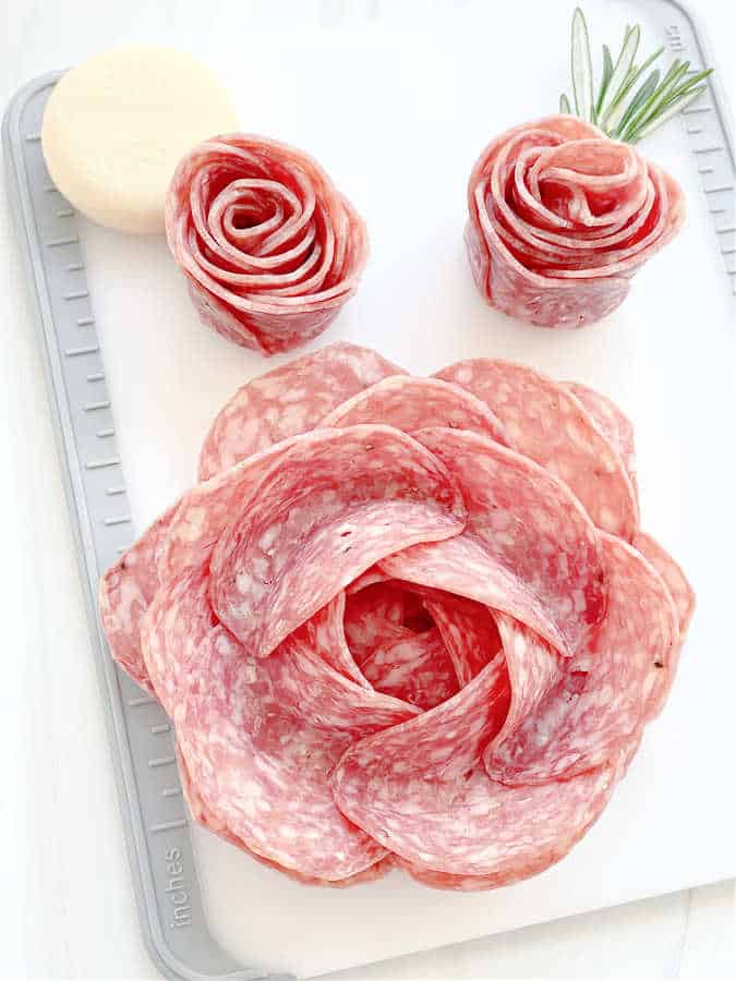 cutting board with a completed large salami rose and two smaller salami rosebuds