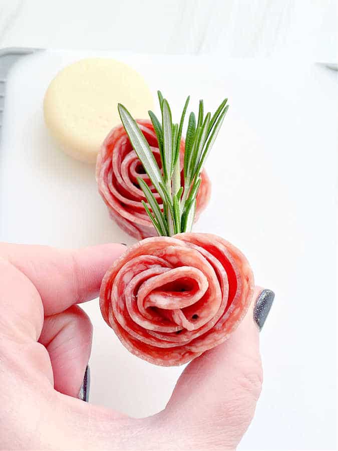 showing a salami rosebud secured with a sprig of rosemary