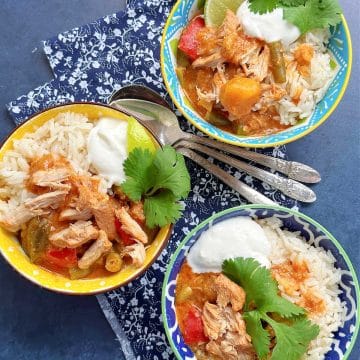 three bowls of pork curry served over coconut jasmine rice and garnished with yogurt, lime wedge and cilantro