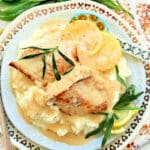 tarragon chicken plated over mashed potatoes and garnished with fresh tarragon and lemon slices