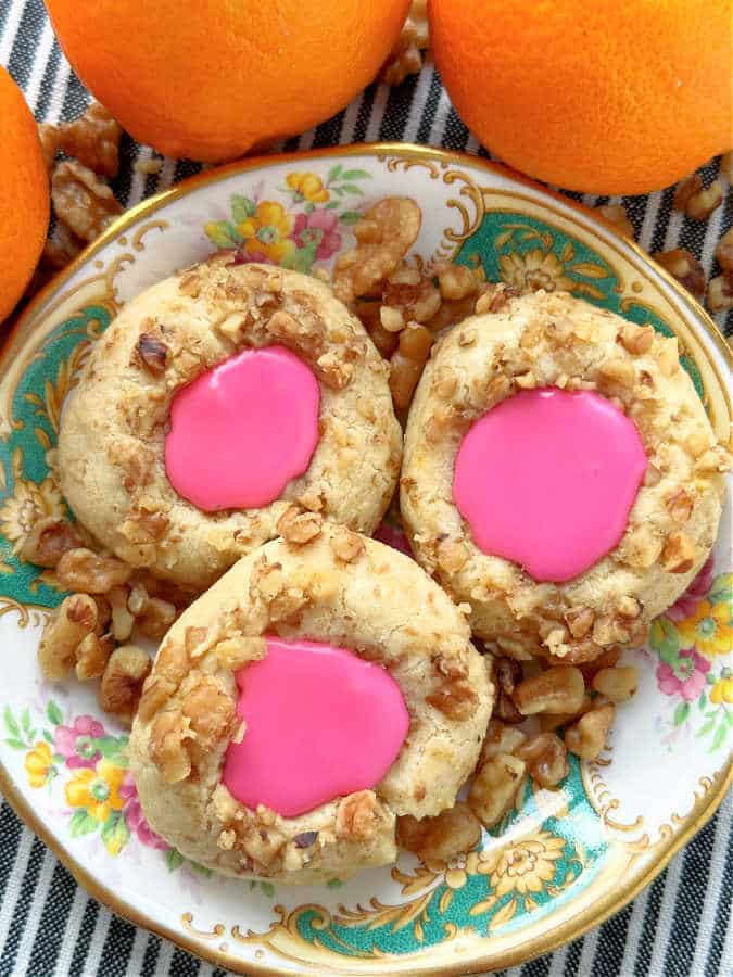 thumbprint cookies with icing plated with walnuts and fresh oranges in the background