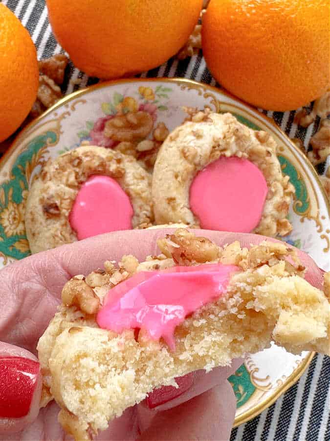 taking a bite of thumbprint cookies with icing frosted with pink frosting